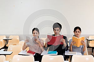 Group of three students reading book together in classroom