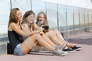 Group of three teenager girls laughing while watching the smart phone