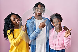 Group of three young black people standing together over pink background with a big smile on face, pointing with hand finger to