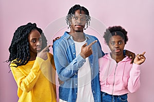 Group of three young black people standing together over pink background pointing with hand finger to the side showing