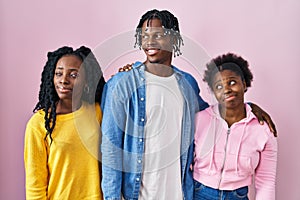 Group of three young black people standing together over pink background smiling looking to the side and staring away thinking