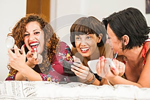 Group of three young cheerful caucasian women  have fun at home during make up activity - laughing girls in friendship making up