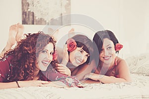 Group of three young cheerful women have fun together laying on the bed ready to go out for the night life - beauty and make up