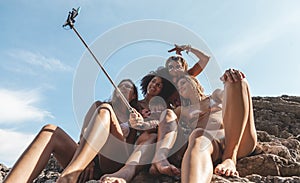 Group of three young multiracial female friends taking a selfie on a rock in the middle of the sea