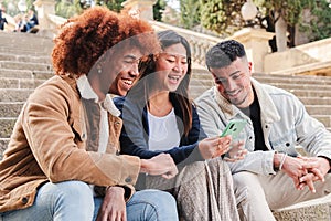 Group of three young multiracial friends smiling and having fun using a social media app on smartphone. Happy teenagers