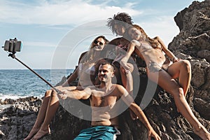 Group of three young multiracial friends taking a selfie on a rock in the middle of the sea