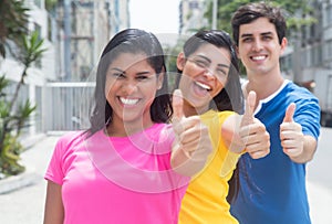 Group of three young people in colorful shirts standing in line and showing thumbs