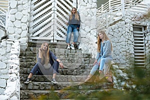 Group of three young Stylish nice girls in pantsuit costumes sitting on a stairs near white construction
