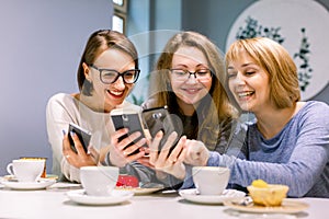 Group of three young women smiling and showing the pictures on the smartphones each other, sitting in restaurant