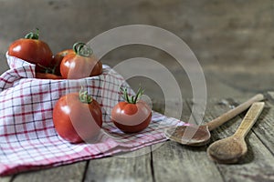 Group of tomatoes in basket with dishcloth and wodden spoons on