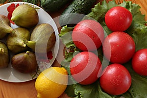 Group of tomatoes with water drops on a lettuce leaves. Lemon, cucumbers and figs in a porcelain plate on a wooden table