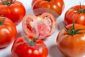 a group of tomatoes on a white background, with shadows. One tomato cut, studio photo, isolate, tomatoes washed