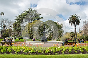 Group of tourist visitors relaxing and resting on the chair around a large cast iron fountain in Albert Park.