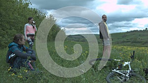 A group of tourists arranged a pass to rest on a beautiful glade. Young beautiful cyclists are resting on nature. Thick