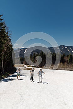 Group of tourists in casual clothes walking on the snow in spring in a mountain resort against the backdrop of beautiful scenery