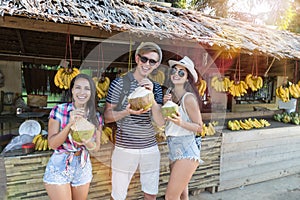 Group Of Tourists Drinking Coconut On Thailand Street Market, Cheerful Man And Women In Traditional Fruits Bazaar In