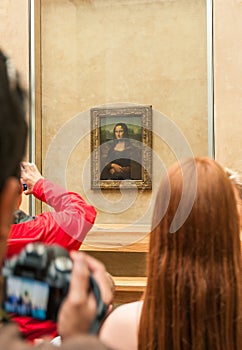 Group of tourists gathered around the Mona Lisa in the Louvre Museum.