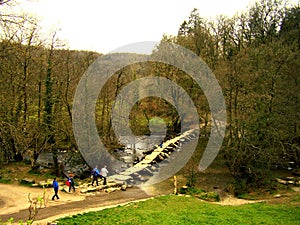 A group of tourists hiking, cross the ancient Tarr Steps Bridge.