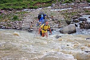 A group of tourists passes a rough mountain river for a wade.