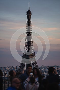 Group of tourists taking photos near the iconic Eiffel Tower in the evening in Paris