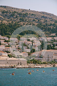 A group of tourists travel in pairs kayaks by sea against the backdrop of a cruise ship and the coast, near old town of