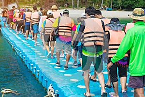 Group of tourists walking on plastic pontoon walk way floating in the sea