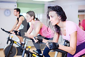 Group training people biking in the gym, exercising legs doing cardio workout cycling bikes