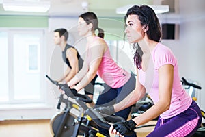 Group training people biking in the gym, exercising legs doing cardio workout cycling bikes