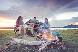 Group of travelers camping and doing picnic and playing music together. Mountain and lake background. People and lifestyle.