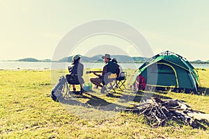 Group of travelers camping and doing picnic and playing music together. Mountain and lake background. People and lifestyle.