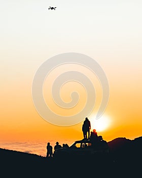 Group of travelers content creators stand by 4wd vehicle together outdoors in nature adventure watch sunset over horizon over