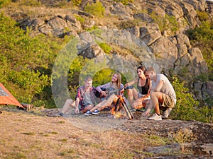 Group of travelers relaxing on a natural background. Friends near fireplace with a guitar. Camping concept. Copy space.