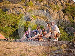 Group of travelers relaxing on a natural background. Friends near fireplace with a guitar. Camping concept. Copy space.