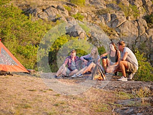 Group of travelers relaxing on a natural background. Friends near fireplace with a guitar. Camping concept. Copy space.