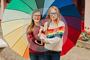 Group of two cute little girls playing outside under big colorful umbrella