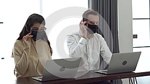 Group of two operator man and woman wearing protective face mask working with headset and laptop computer in a call centre .