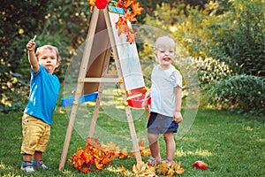 Group of two white Caucasian toddler children kids boy and girl standing outside in summer autumn park by drawing easel