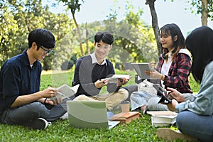 Group of university students reading book on green lawn at university campus. Youth lifestyle, university and friendship