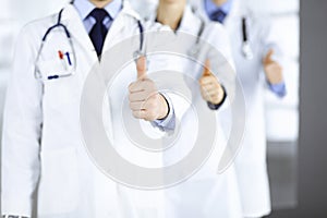 Group of unknown doctors stand as a team with thumbs up in a hospital office. Physicians ready to examine and help