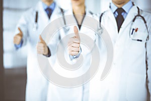 Group of unknown doctors stand as a team with thumbs up in a hospital office. Physicians ready to examine and help