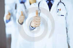 Group of unknown doctors stand as a team with thumbs up in a hospital office. Physicians ready to examine and help