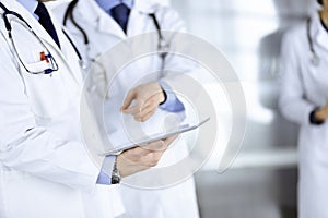 Group of unknown doctors use a computer tablet to check up some medical names records, while standing in a hospital