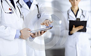 Group of unknown doctors use a computer tablet to check up some medical names records, while standing in a hospital