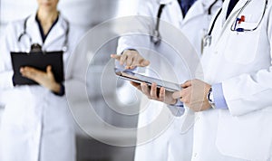 Group of unknown doctors use a computer tablet to check up some medical names records, while standing in a hospital