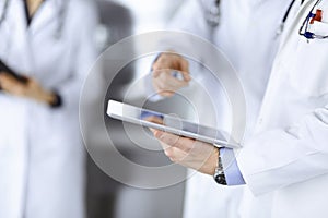 Group of unknown doctors use a computer tablet to check up some medical names records, while standing in a hospital