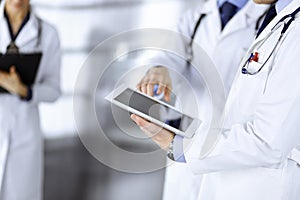 Group of unknown doctors use a computer tablet to check up some medical names records, while standing in a hospital