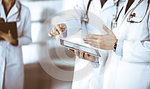 Group of unknown doctors use a computer tablet to check up some medical names records, while standing in a hospital