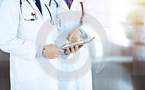 Group of unknown doctors use a computer tablet to check up some medical names records, while standing in a sunny
