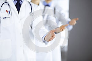 Group of unknown modern doctors stand as a team with open hands in a hospital office. Physicians ready to examine and