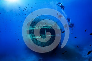 A group of unrecognizable divers explore a sunken shipwreck